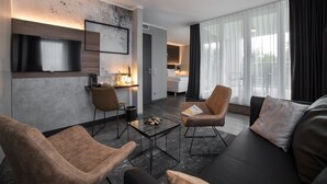 Una habitación de hotel moderna con zona de estar que incluye un sofá, dos sillones, una mesa de centro y un televisor de pantalla plana montado en la pared.