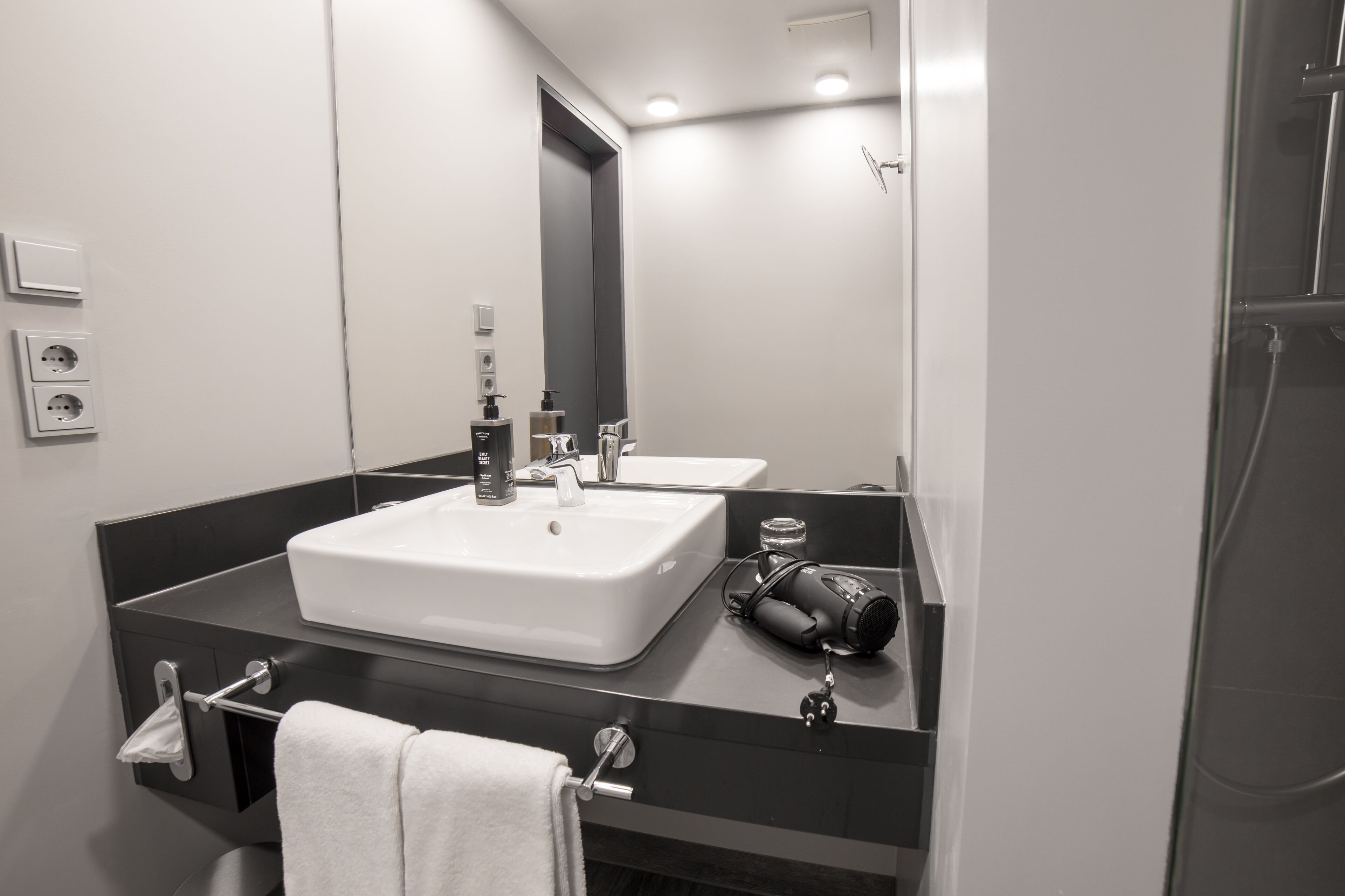Un baño moderno con un lavamanos blanco grande, un espejo y un secador de pelo en la encimera.