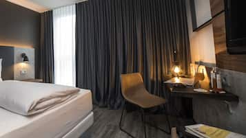 Una habitación de hotel con cama, escritorio con lámpara, silla, televisor y ventana con cortinas.