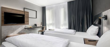 A hotel room with two beds, a desk with a laptop, a flat-screen TV mounted on the wall, and a large window with curtains.