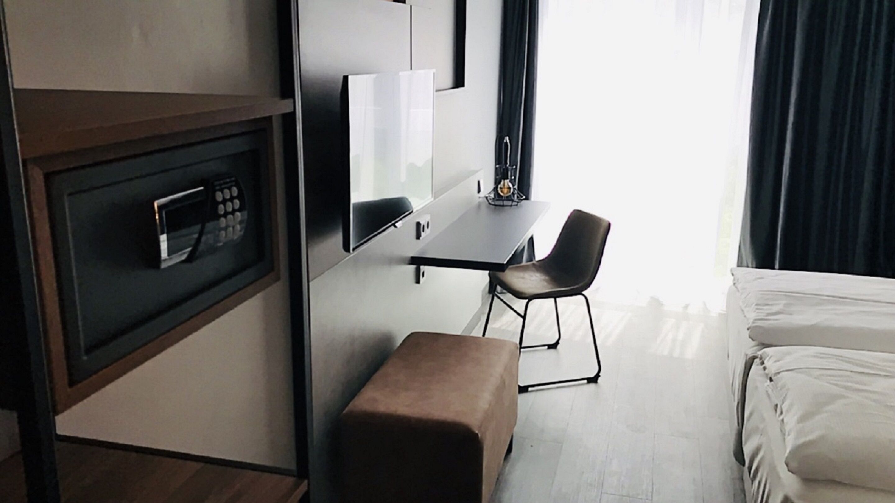A modern hotel room with a bed, a desk, a chair, a microwave, and a small bench.