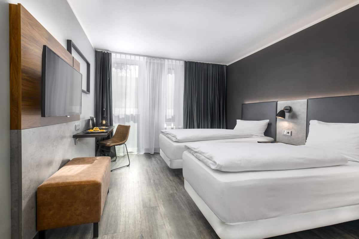 A modern hotel room with two beds, a desk with a chair, a small bench, and a large window with curtains.