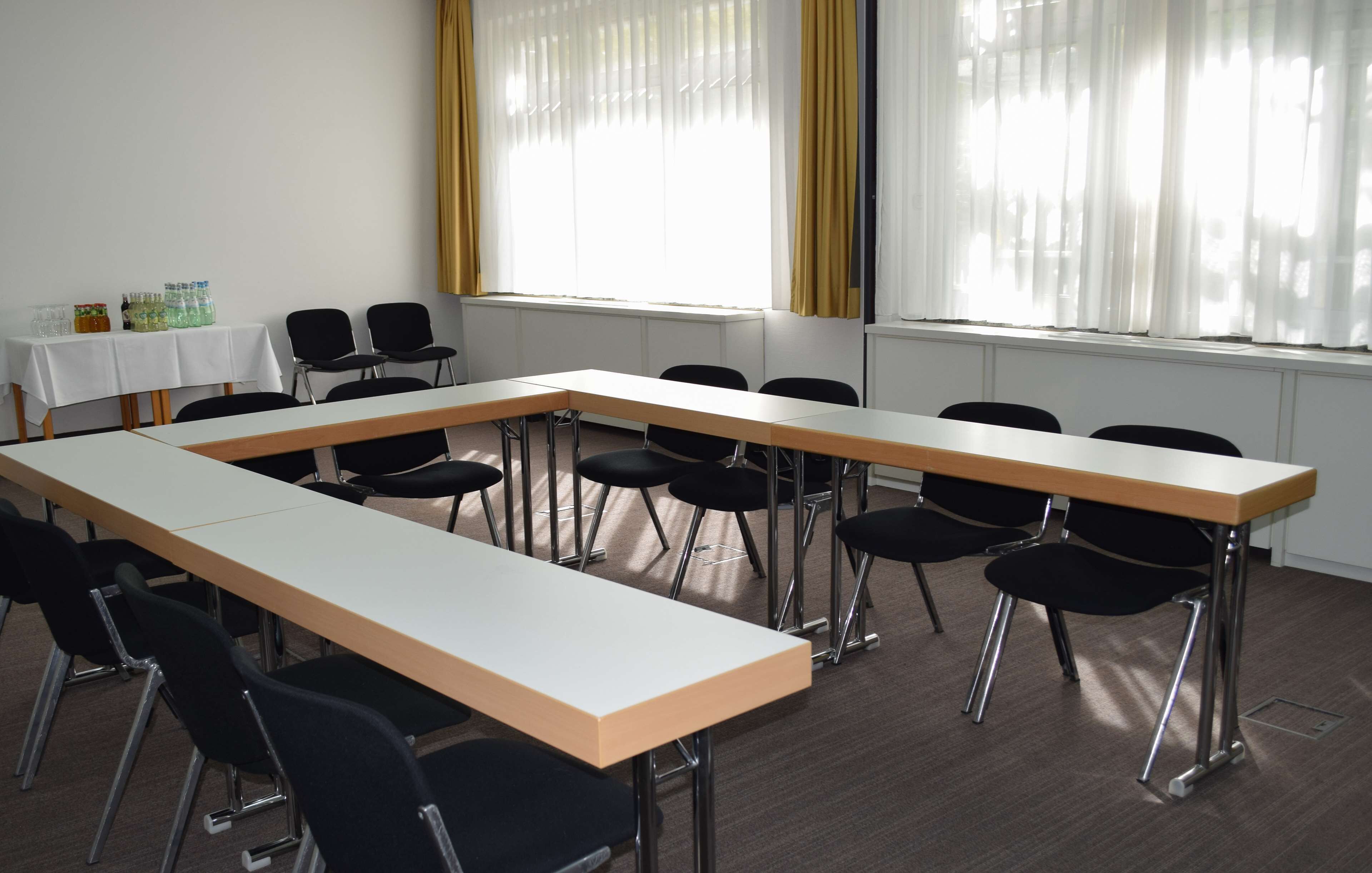 A conference room with a long table, black chairs, a white tablecloth, and a window with yellow curtains.
