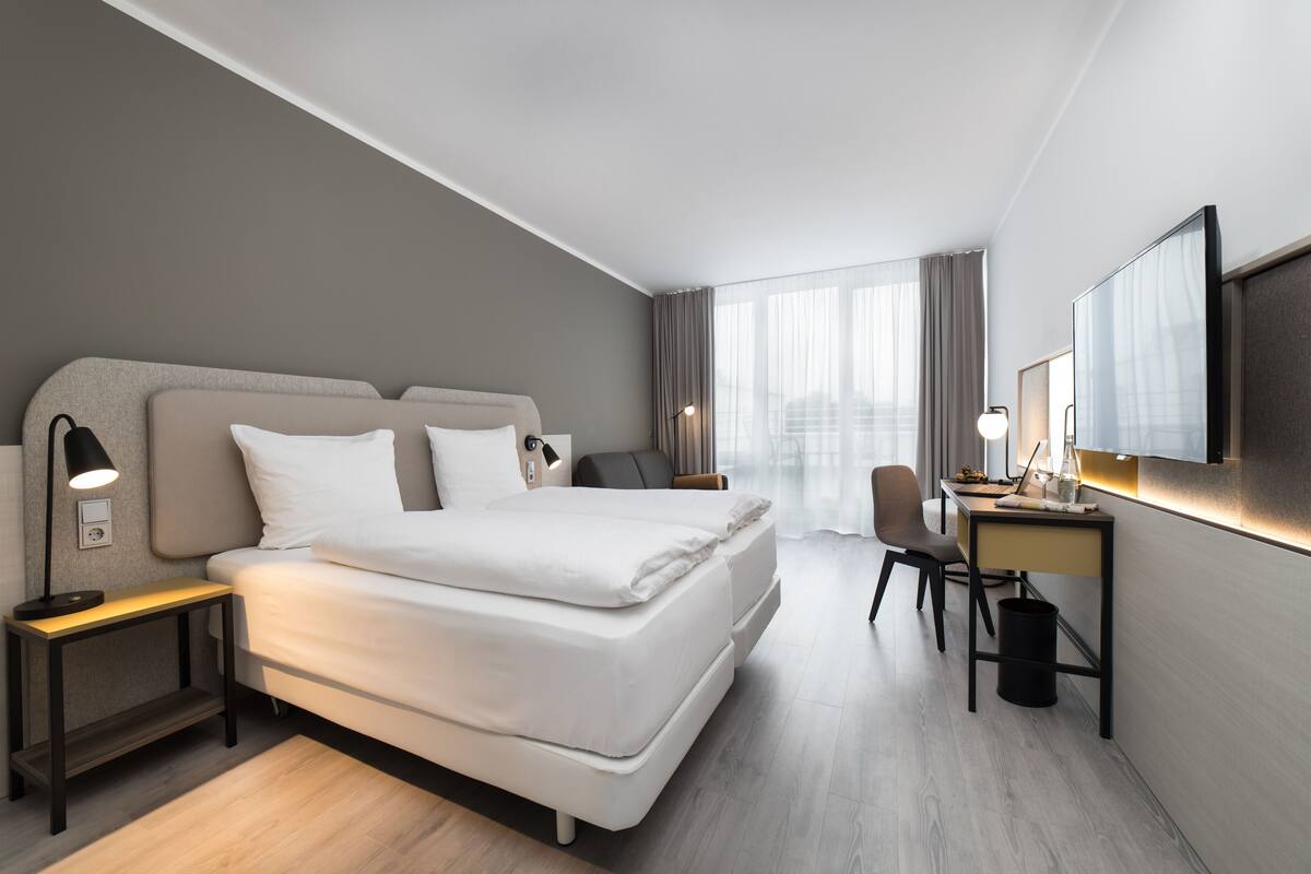A modern hotel room with a large bed, a desk, a chair, and a TV.