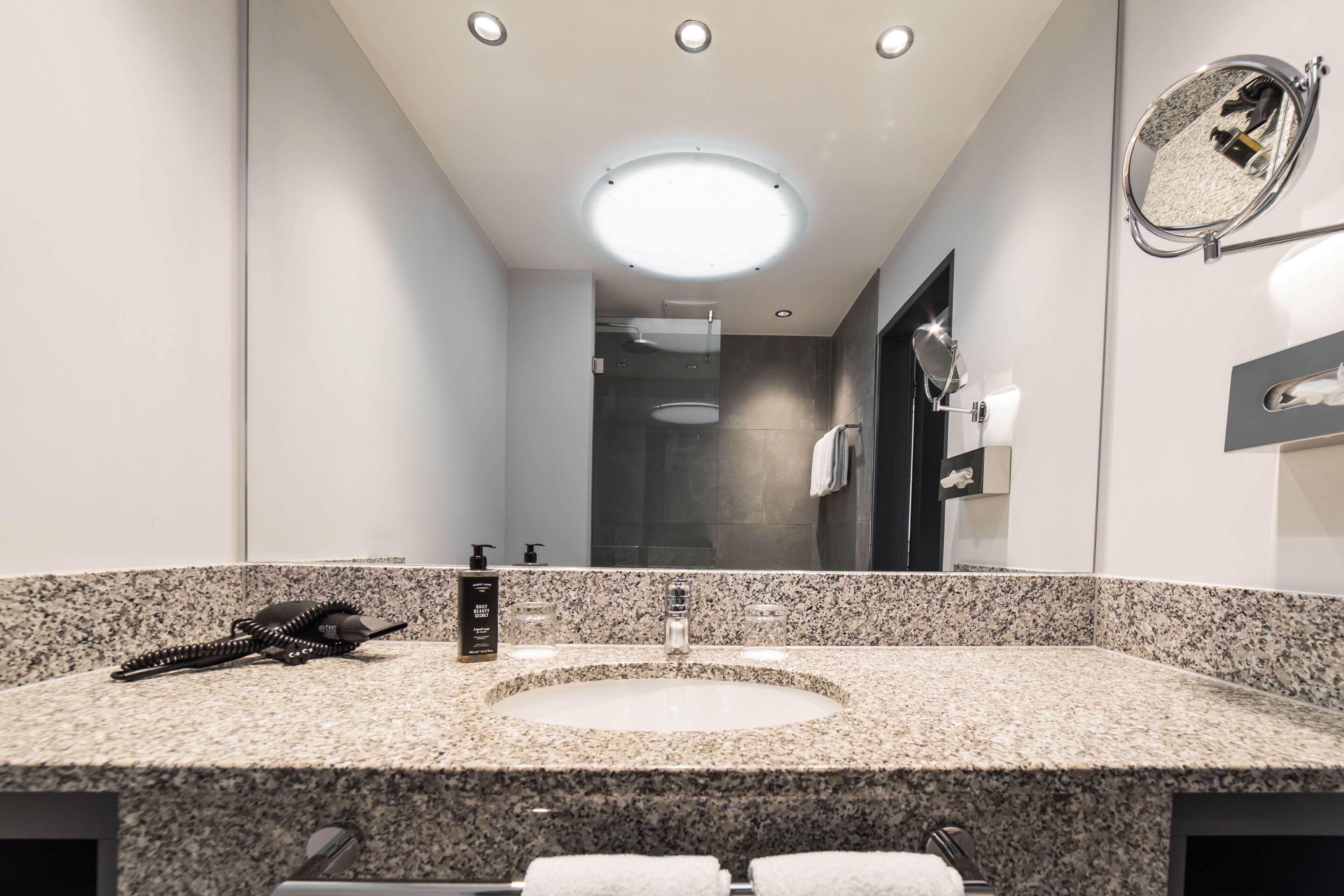 A modern bathroom with a granite countertop, a round sink, a handheld phone, and a mirror with a round frame.