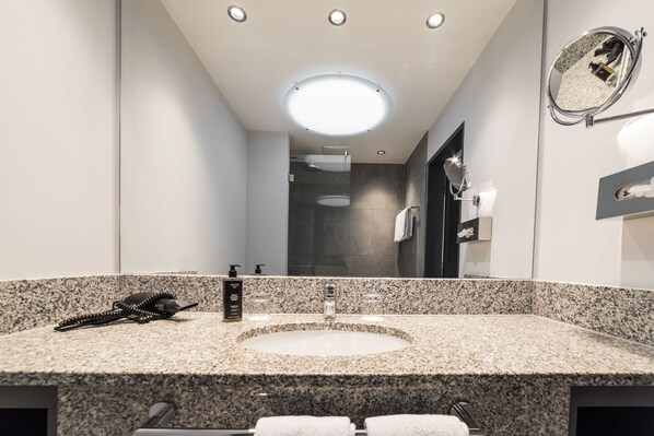 A modern bathroom with a granite countertop, a round sink, a handheld phone, and a mirror with a round frame. - SCOTTY + PAUL Hotel Deggendorf (Deggendorf)