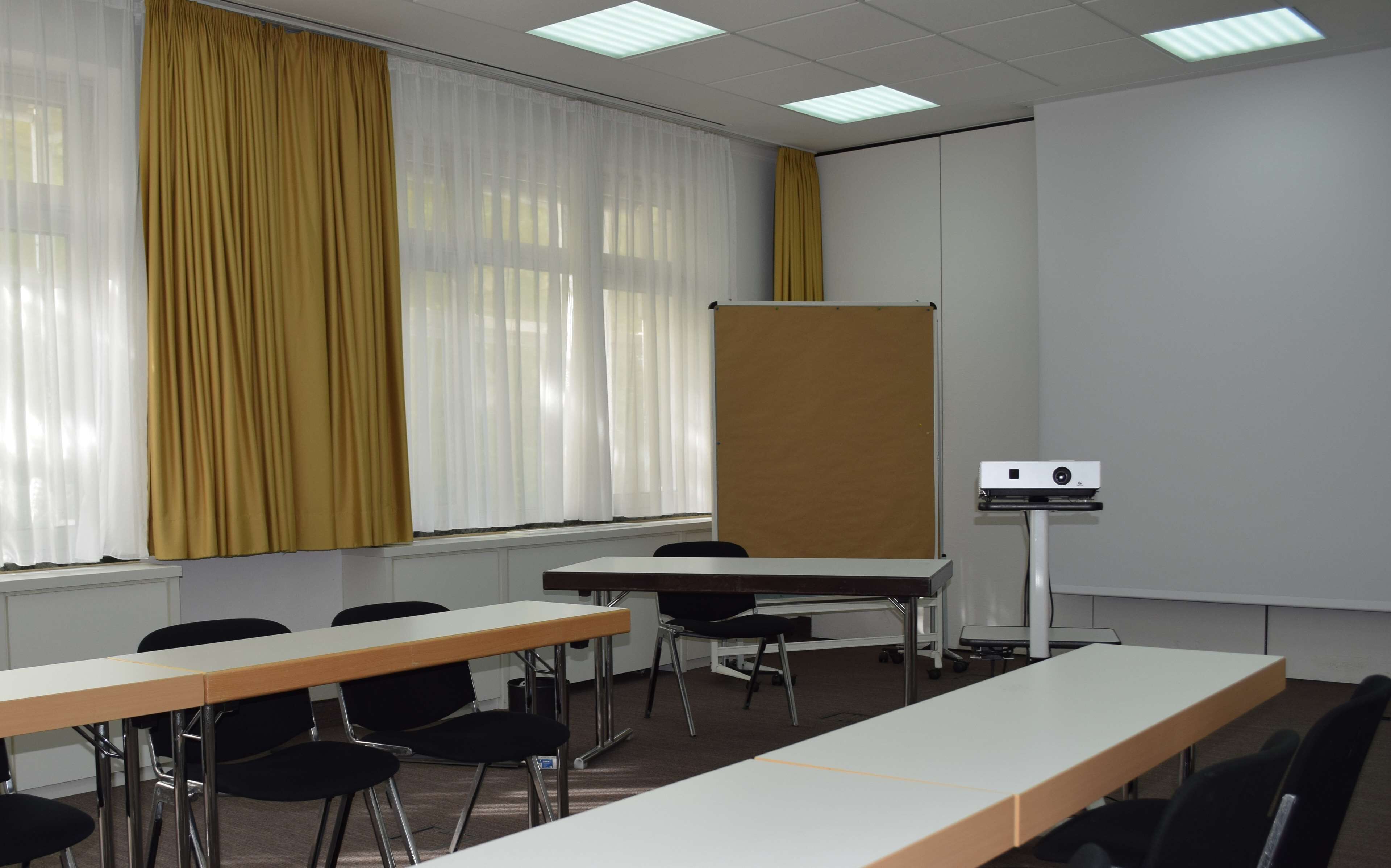 Un salón de conferencias con una larga mesa, sillas, un proyector y una pizarra.