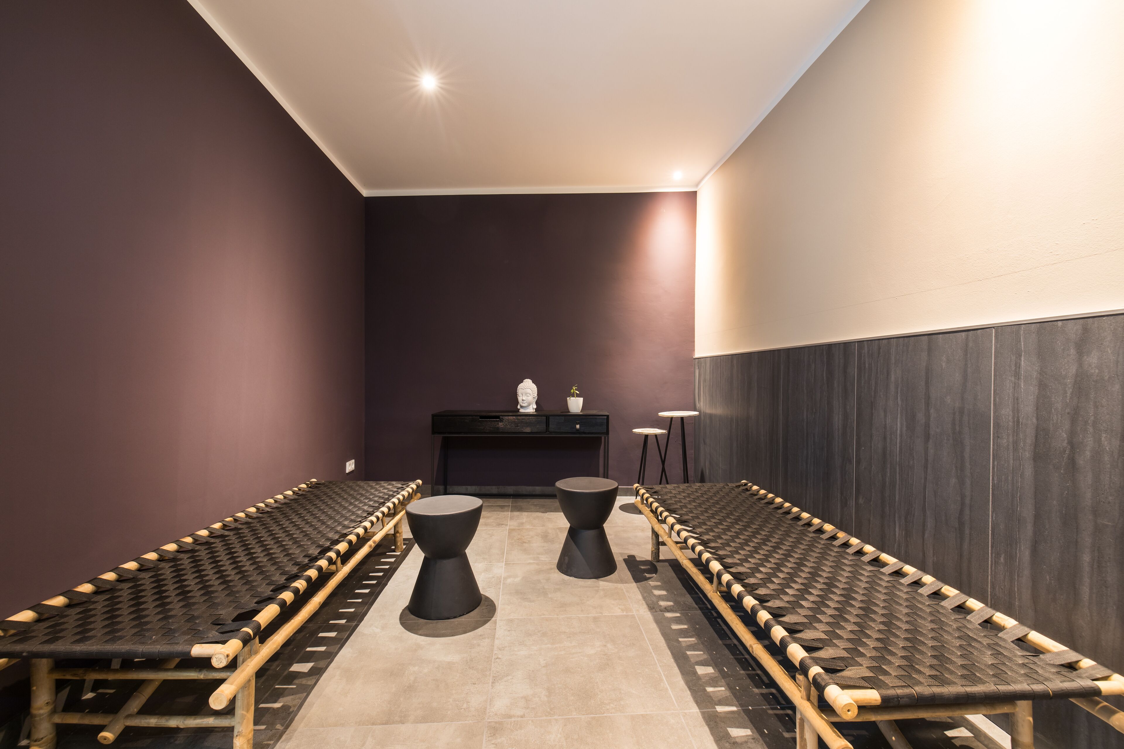 A room with a long, narrow bench seating arrangement, a central table, and a dark-colored wall.