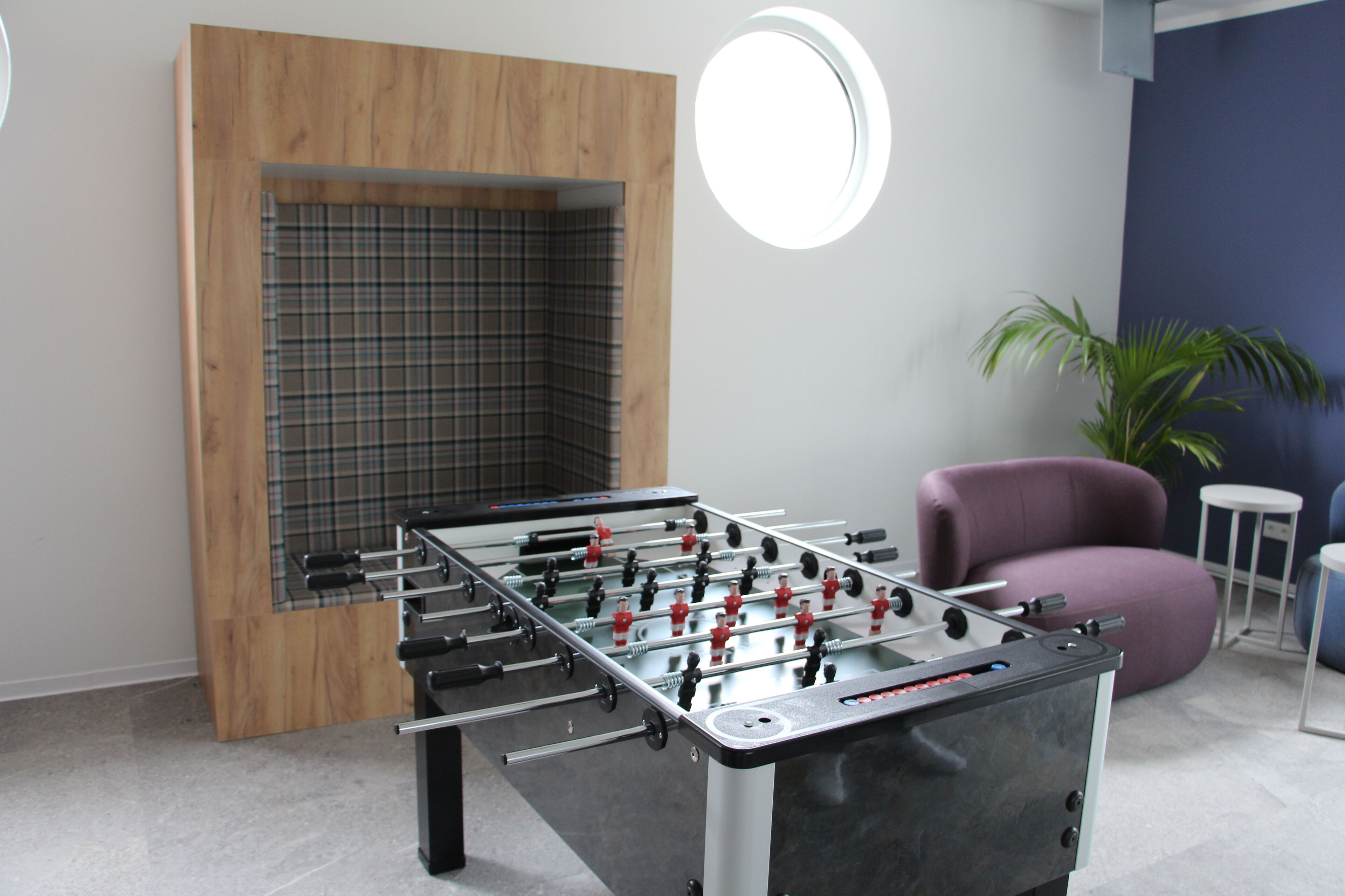 A foosball table in a room with a wooden accent wall, a purple chair, and a small round table.