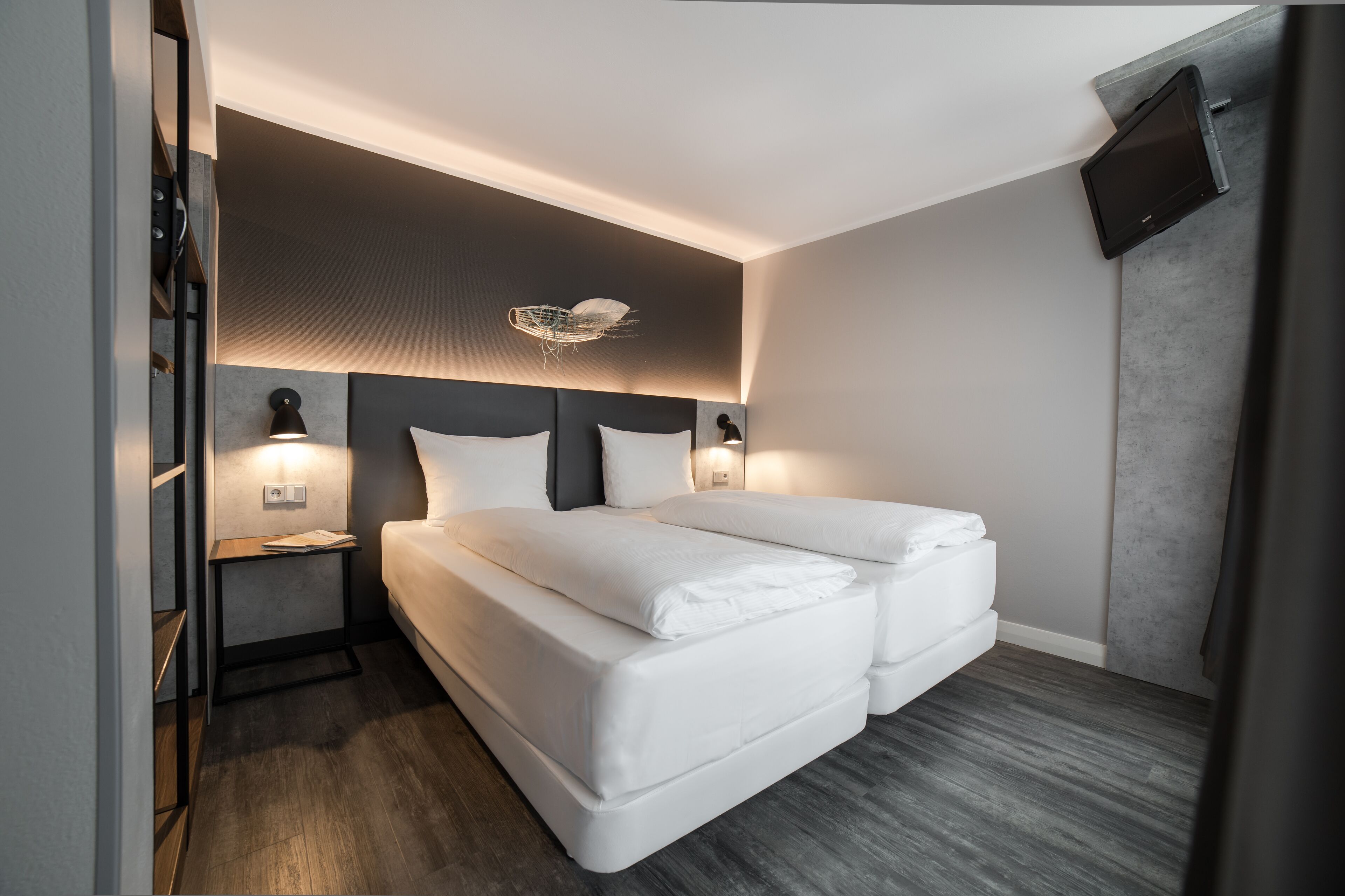 Una habitación de hotel moderna con una cama doble, mesitas de noche, un televisor montado en la pared y una lámpara de techo original.