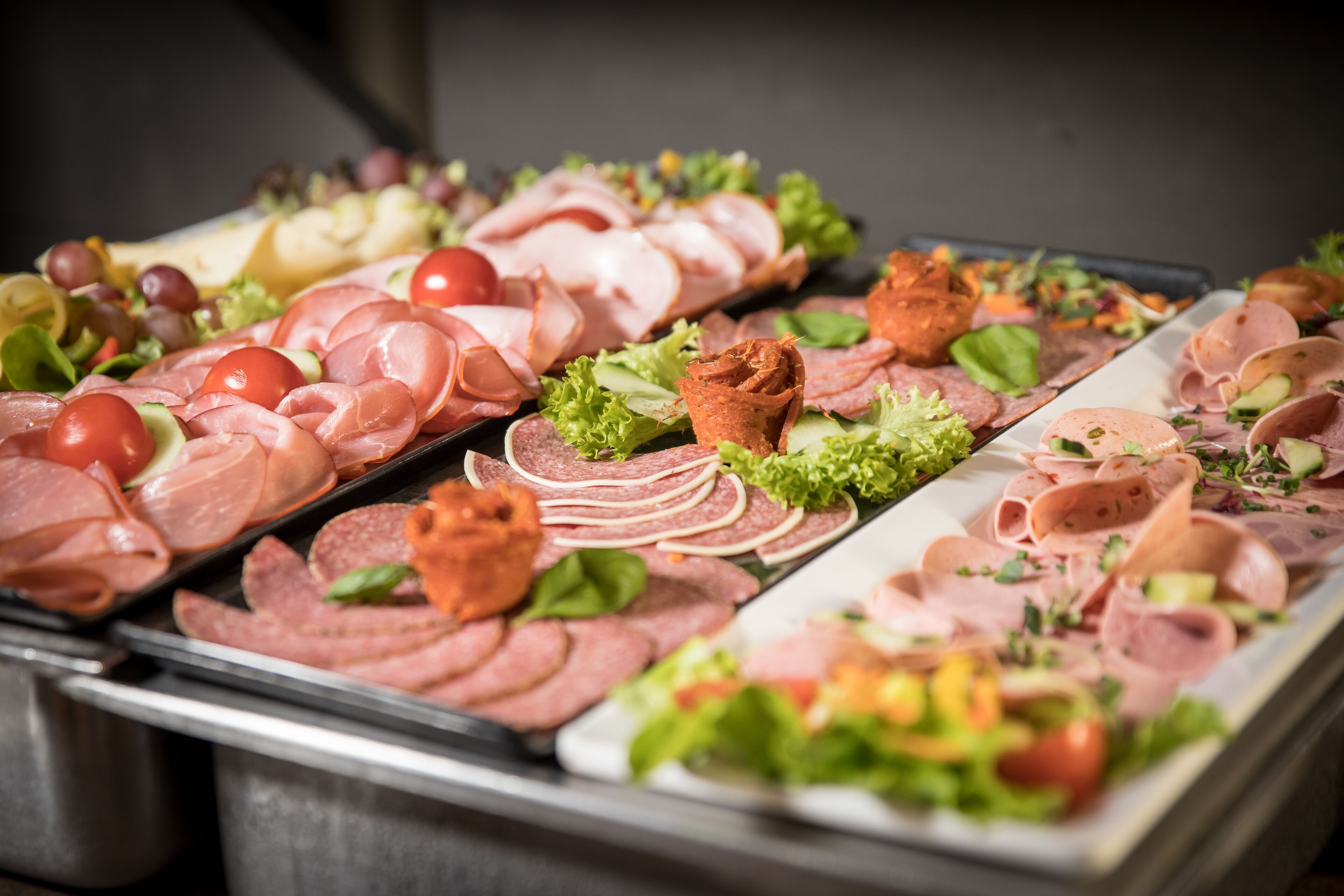 A buffet with various types of sliced meats, cheeses, and garnishes.