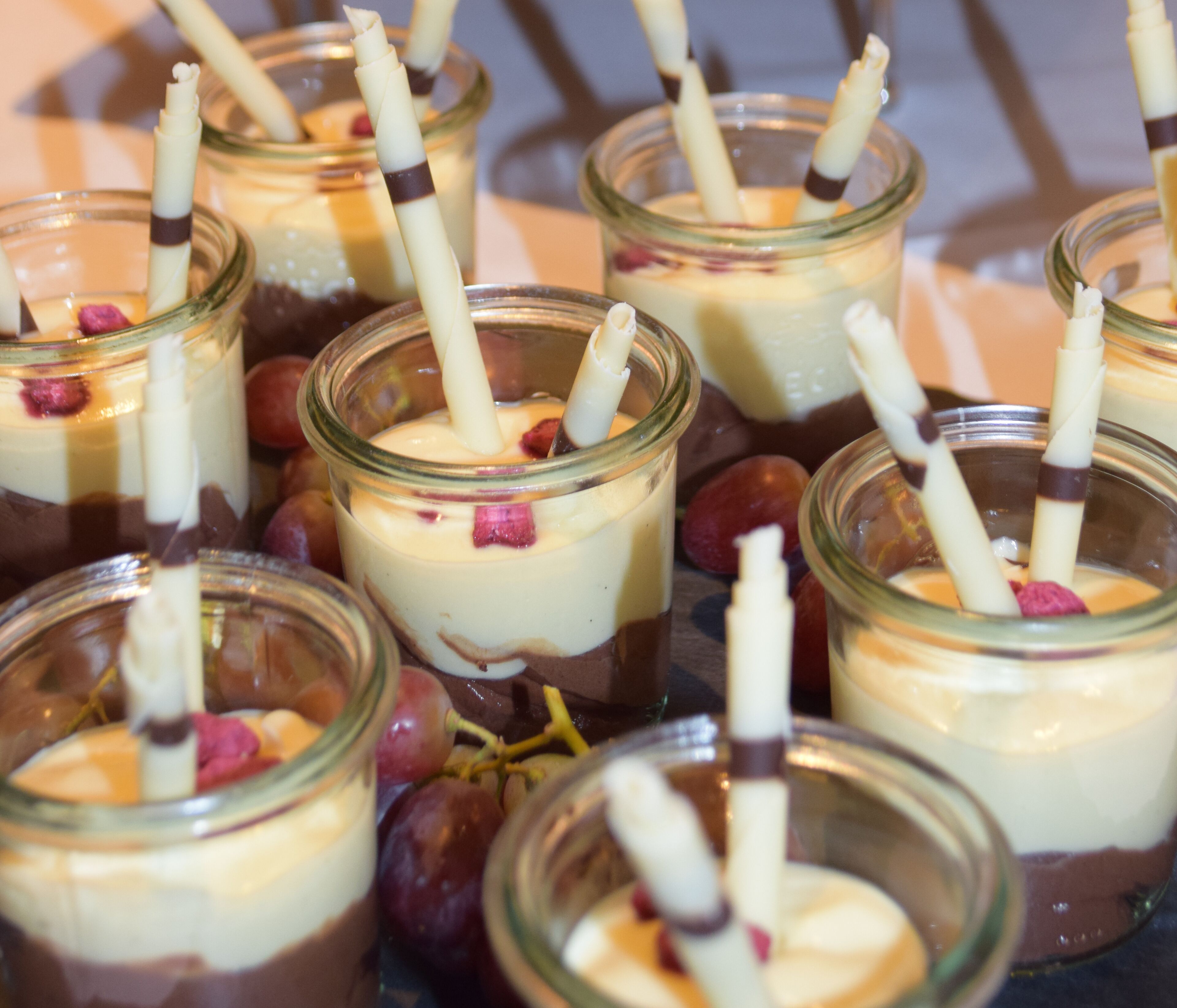 Several glass jars containing layered desserts with chocolate sticks, surrounded by grapes.