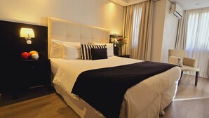 A hotel room with a large bed, a nightstand with a lamp, a chair, and a view of the outdoors through the window. - Ulises Recoleta Suites (Buenos Aires)