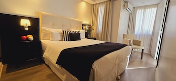 A hotel room with a large bed, a nightstand with a lamp, a chair, and a view of the outdoors through the window.