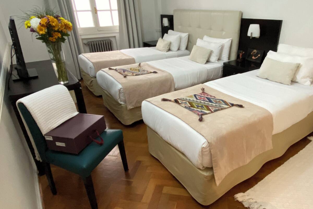 Habitación de hotel con dos camas, una silla, un escritorio, un florero con flores y un espejo.