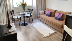 A living room with a beige sofa, two black chairs, a round table with a vase of flowers, a white rug, and a framed picture on the wall. - Ulises Recoleta Suites (Buenos Aires)