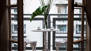 A view through a window with a table and chairs, a vase with green plants, and a building in the background. - Ulises Recoleta Suites (Buenos Aires)