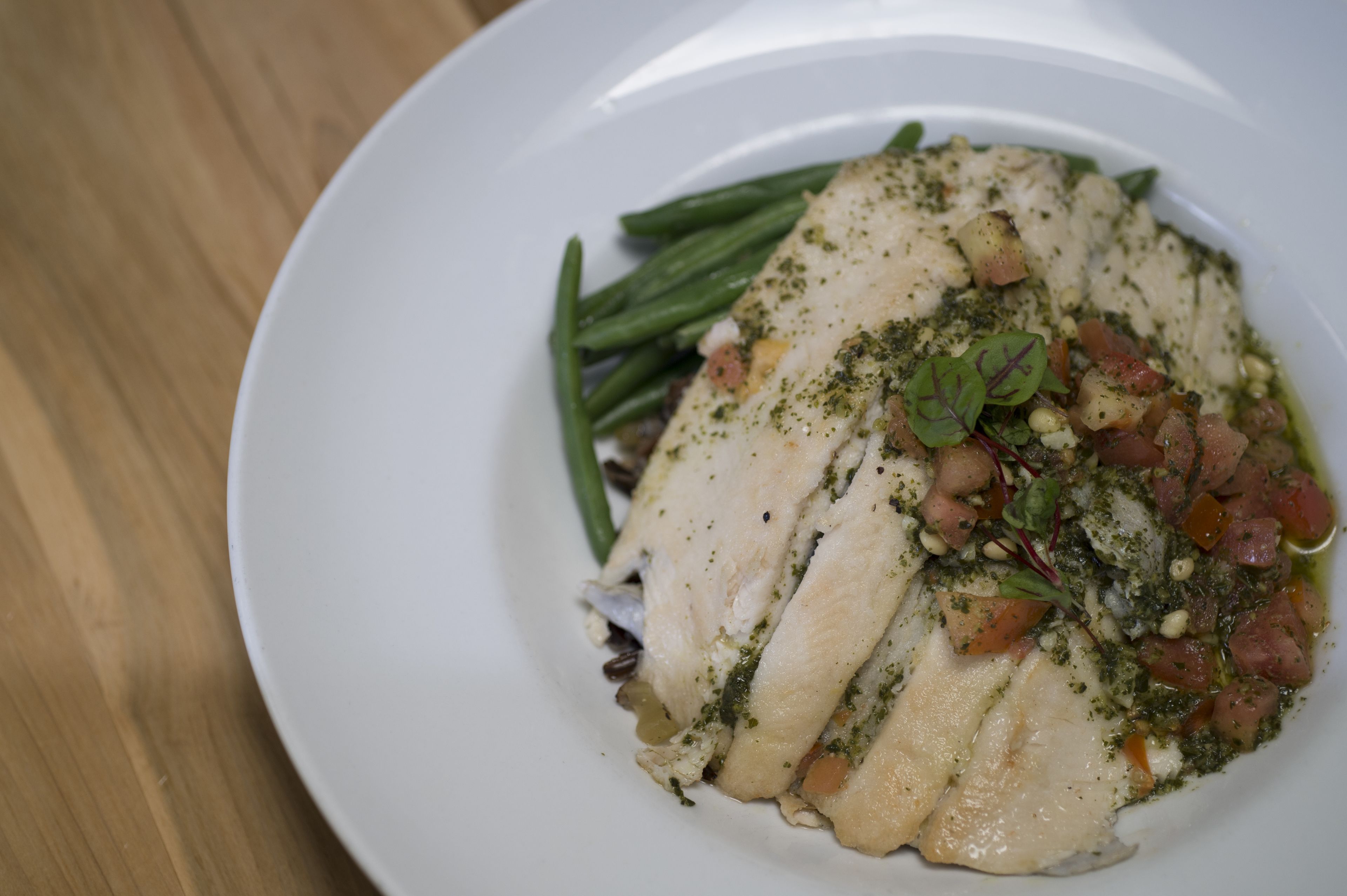 A white plate with a fish fillet, green beans, and a tomato-based topping.