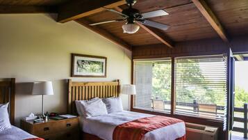 A bedroom with two beds, wooden headboards, a ceiling fan, a framed picture on the wall, and a window with blinds.