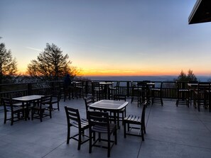 Un patio al aire libre con mesas y sillas, con vistas a un paisaje pintoresco durante el atardecer.