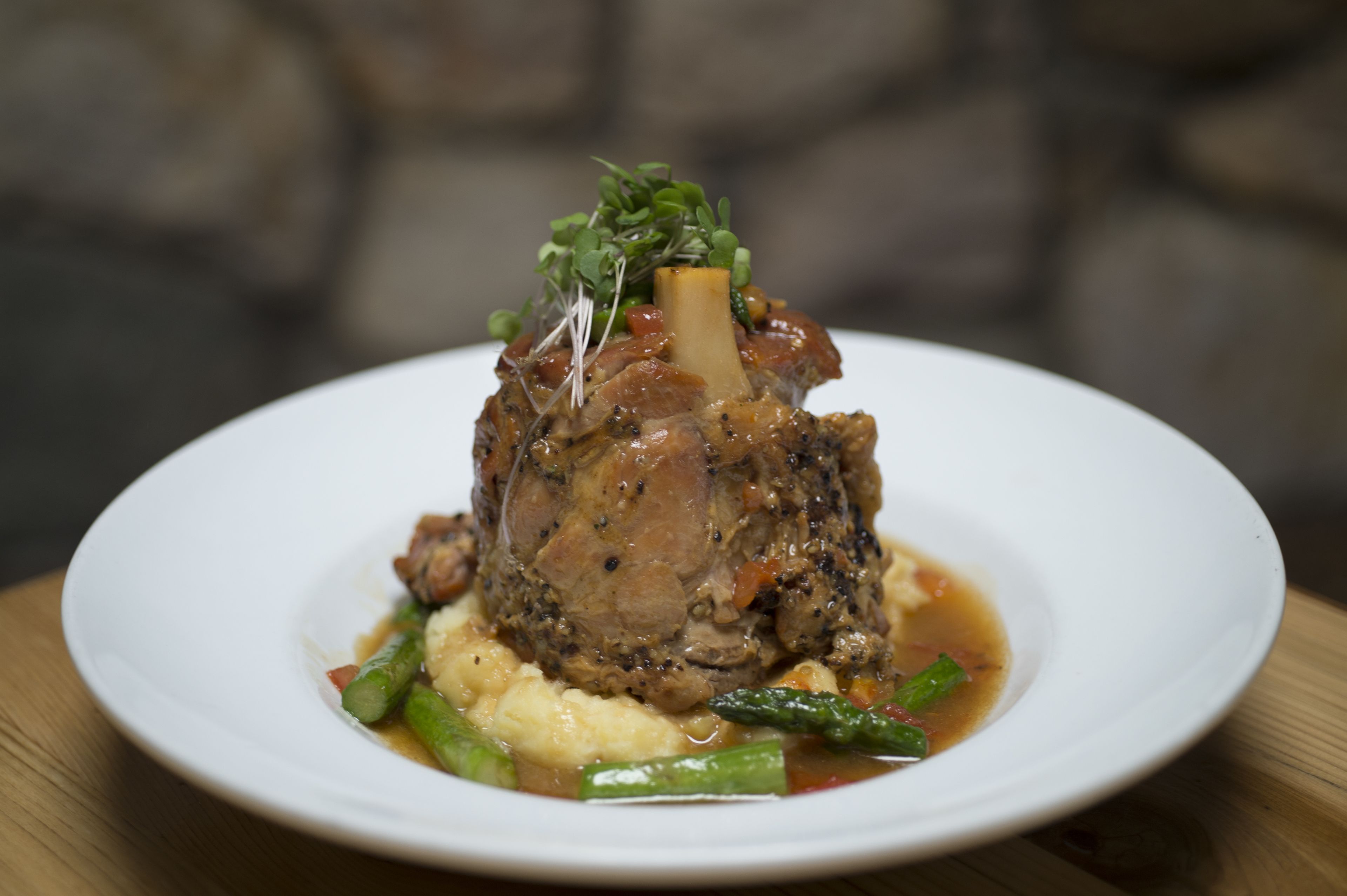 Une assiette contenant un morceau de viande avec un os, des légumes verts et de la purée de pommes de terre.