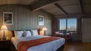 A bedroom with a large bed, two bedside tables, a desk, and a chair. There are two windows with curtains, and the room has wooden walls and ceiling. - Skyland (Luray)