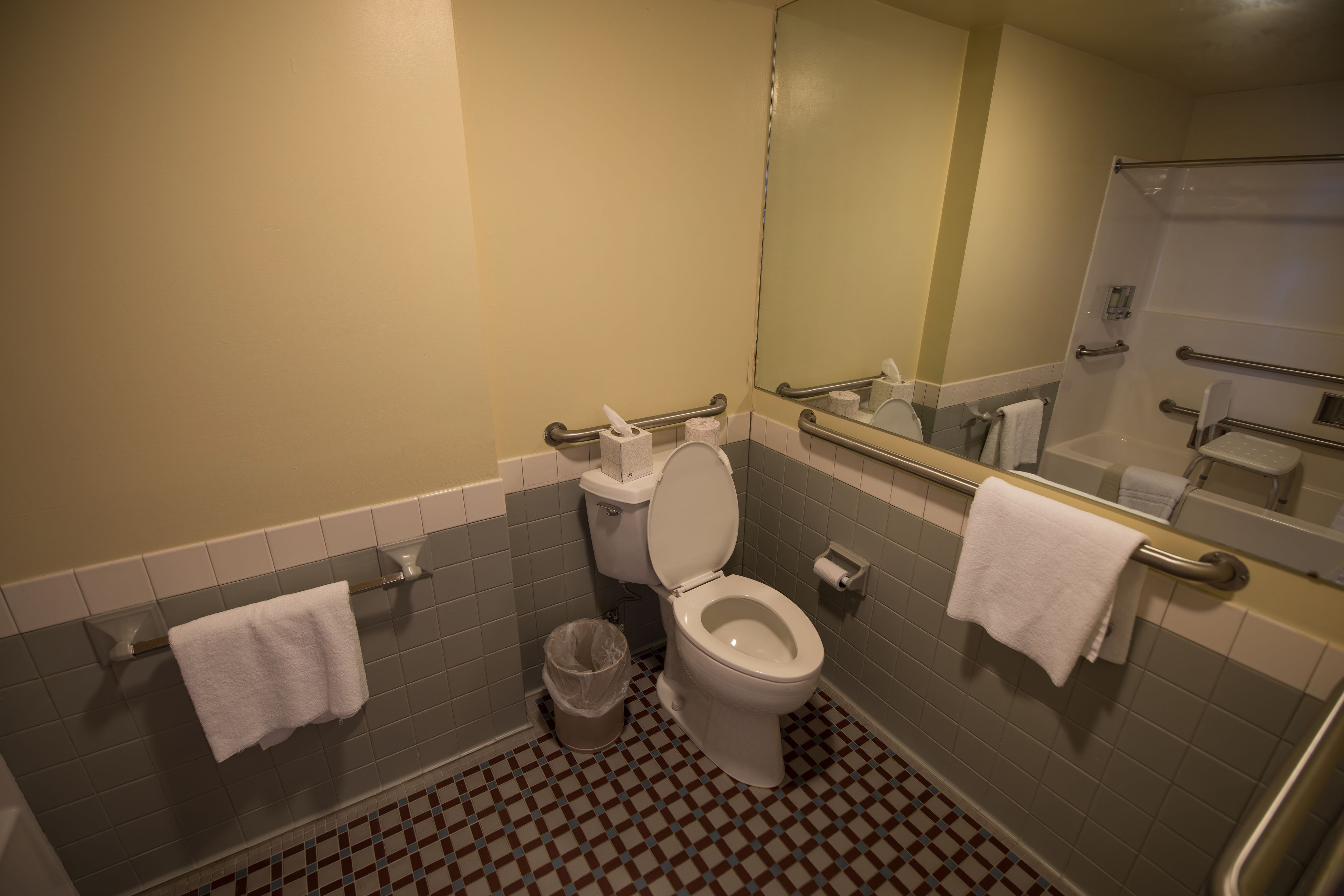 A bathroom with a toilet, two handrails, a trash can, and two towels hanging on towel bars.