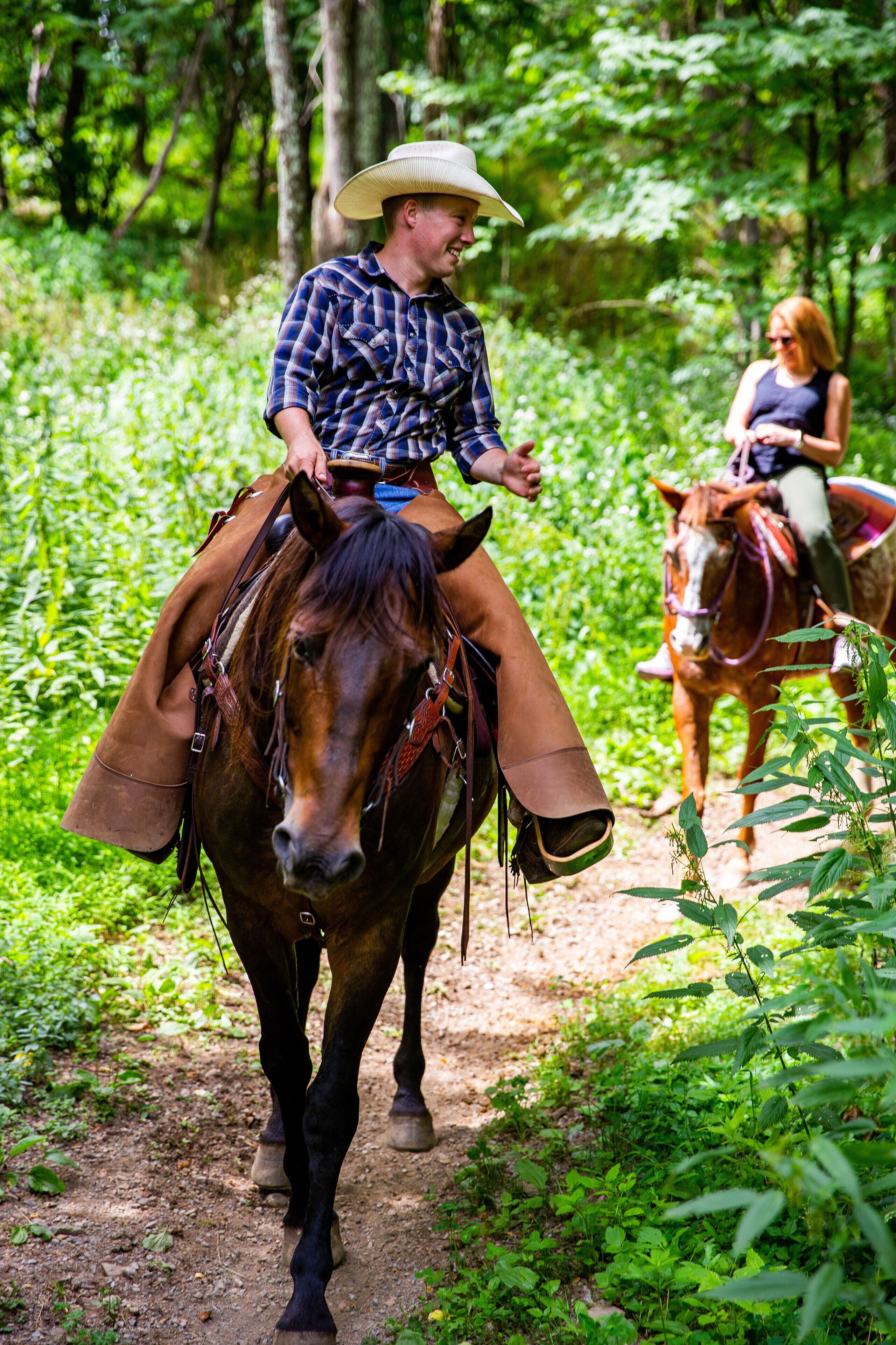 A person riding a horse on a dirt path surrounded by greenery.
