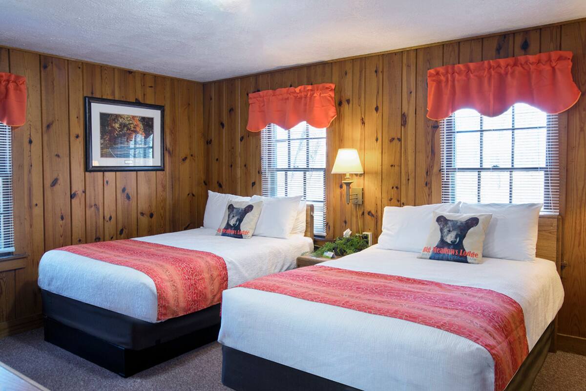 A room with two beds, wooden walls, and a framed picture on the wall.