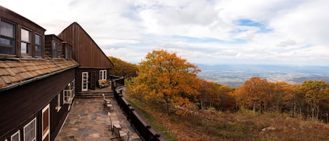 A wooden cabin with a stone patio and a view of autumn foliage and distant landscape.