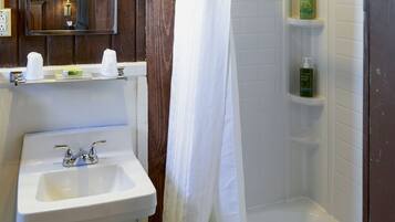 A bathroom with a white sink, a mirror, a shower curtain, and a shelf with toiletries.