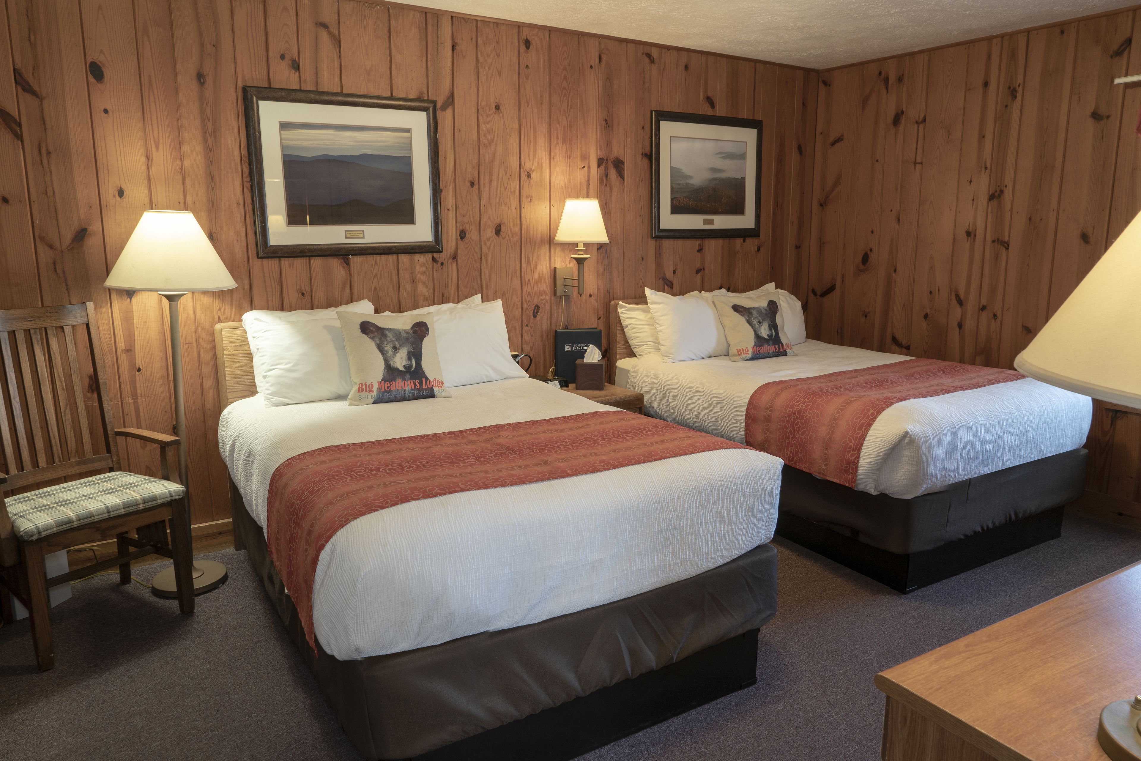 A hotel room with two beds, wooden panel walls, and framed pictures on the wall.