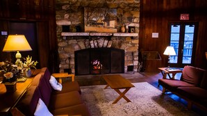 A cozy room with a stone fireplace, wooden furniture, and a view of the outside.