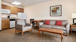 A compact living space with a kitchenette, a gray sofa with red cushions, a wooden coffee table, and a patterned carpet.