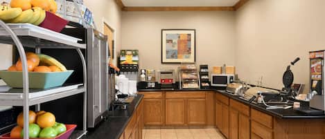 A breakfast bar with fruit, a coffee machine, and a waffle maker.