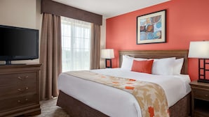A hotel room with a large bed, a television, and a painting on the wall.