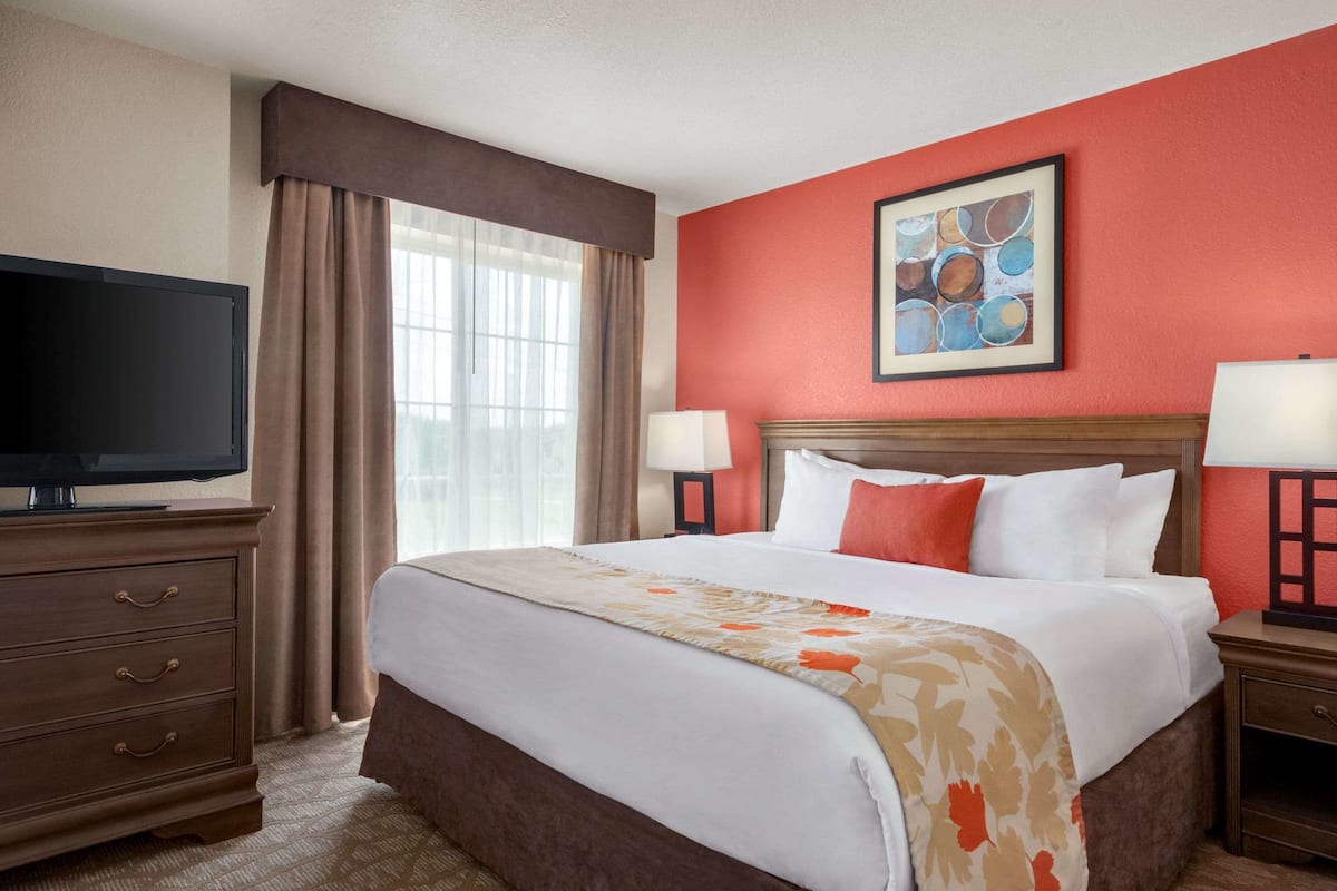 A hotel room with a large bed, a television, and a painting on the wall.