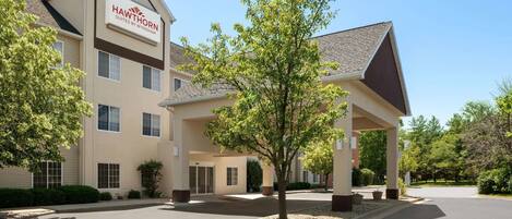 A hotel with a sign reading "Hawthorn Suites by Wyndham" and a covered entrance area with a tree in the center.