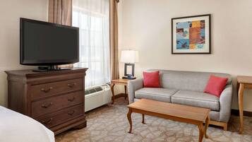 A hotel room with a flat-screen TV, a sofa, a wooden coffee table, a dresser, a lamp, and a painting on the wall.