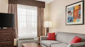 A hotel room with a grey sofa, a wooden table, a TV, a lamp, and a framed artwork on the wall.