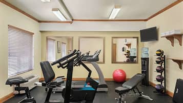 A gym with treadmills, exercise bikes, a bench, and a ball.