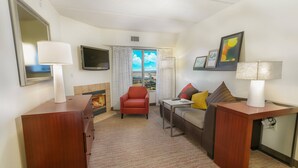 A hotel room with a wooden desk, a red armchair, a sofa with cushions, a flat-screen TV, a fireplace, and a large window with a view. - Residence Inn by Marriott Fort Worth Alliance Airport (Fort Worth)