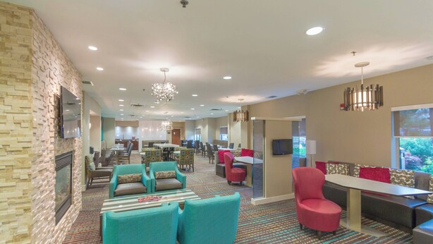 A spacious hotel lobby with a patterned carpet, teal and red seating, a chandelier, and a television on the wall. - Residence Inn by Marriott Fort Worth Alliance Airport (Fort Worth)