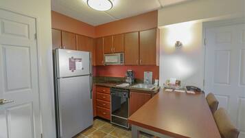 Una cocina compacta con armarios de madera, refrigerador, microondas, lavavajillas y una mesa de comedor con sillas.