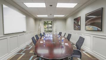A conference room with a large oval table, chairs, water bottles, and a projector screen.