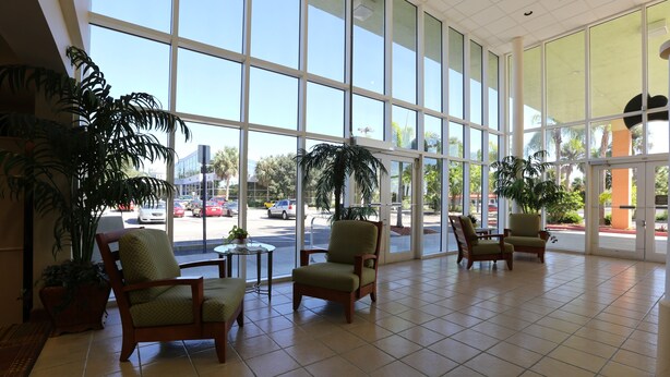 A spacious lobby with large windows, several chairs, and potted plants. - Allure Suites (Fort Myers)