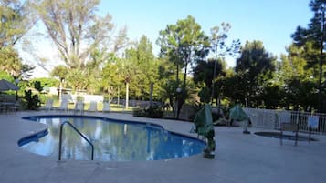A swimming pool with a curved edge, surrounded by a fence and trees.