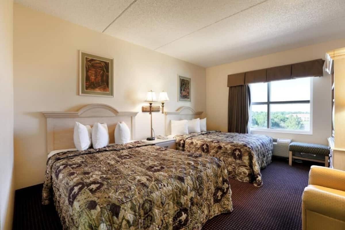 Habitación de hotel con dos camas, un escritorio, una silla y una ventana con cortinas.
