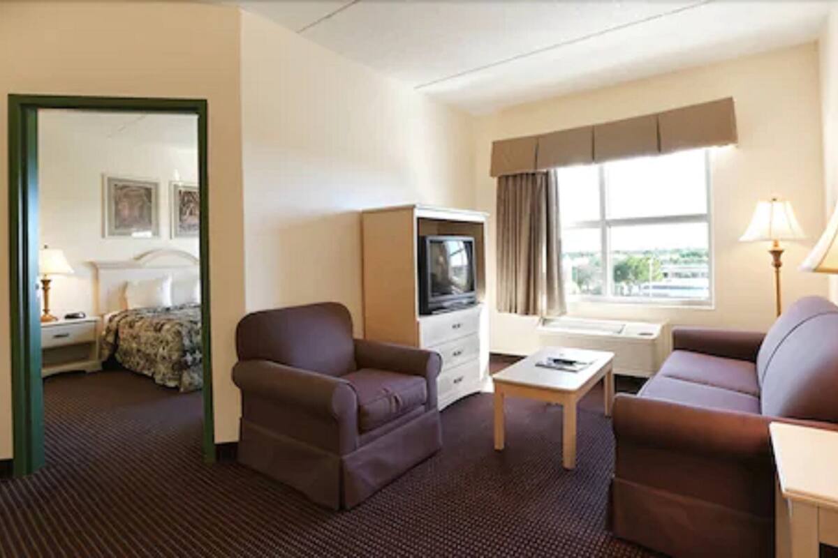 Habitación de hotel con cama, dos sillones, una mesita, televisor y ventana con cortinas.