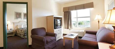 A hotel room with a bed, two armchairs, a small table, a TV, and a window with curtains.